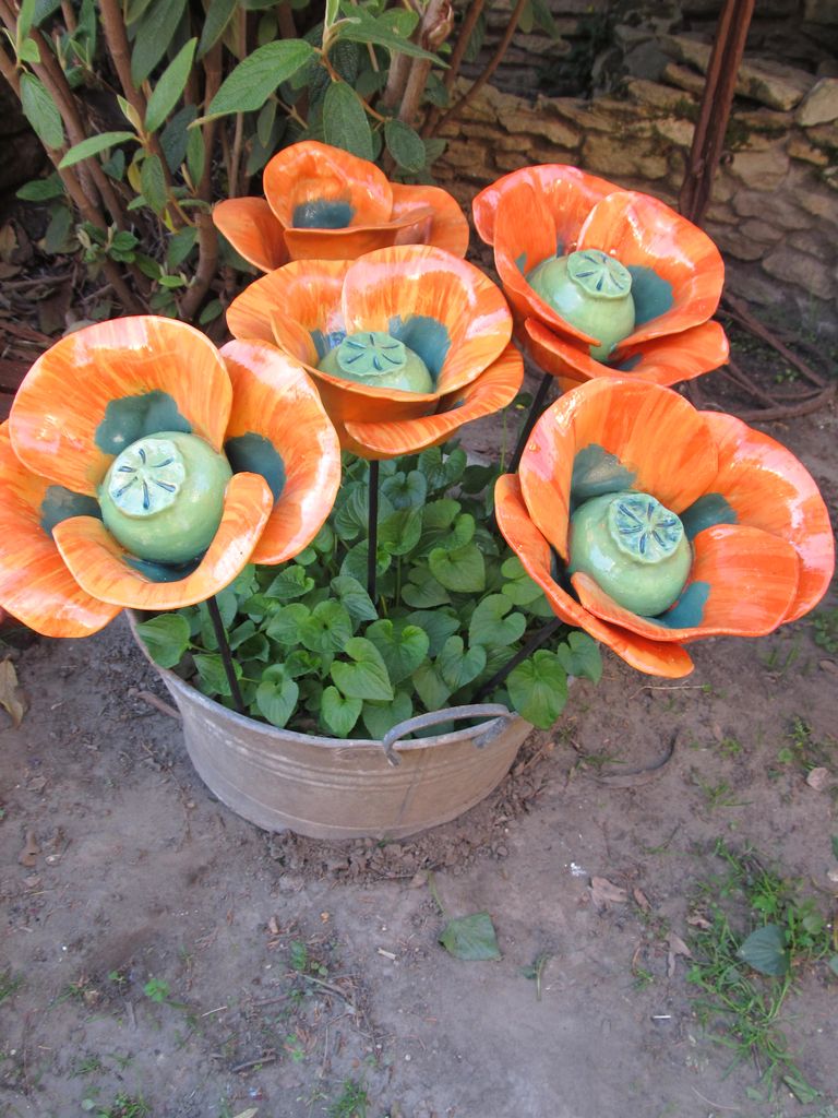 Vas szárú, pipacs formájú kerámia virágok élénk narancs színben, egy dézsába szúrva.