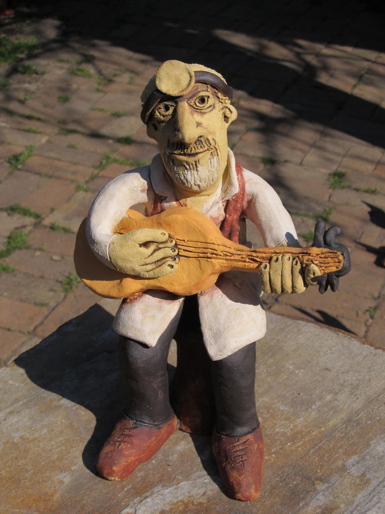 Kerámia figura, szakállas orvos gitárral a kezében, a fején gégész tükörrel.